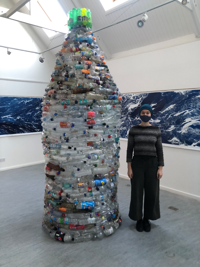Person standing next to gaiant scupture made out of waste plastic bottles.